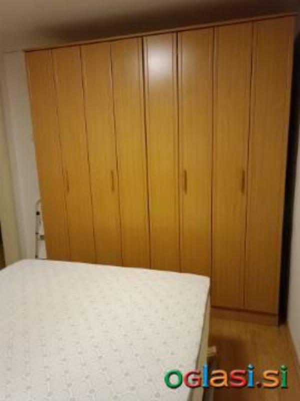 Garderobna omara, postelja z vzmetnico in nad vložek plus mizica.